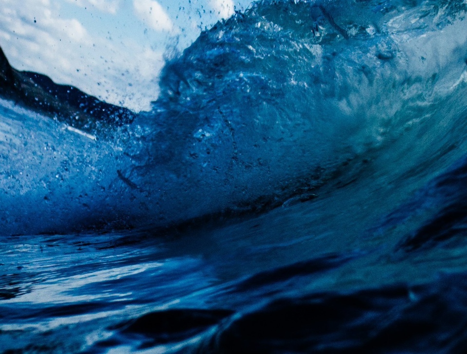 Photo taken in the sea, showing crashing blue waves against a blue sky, photo by Tim Marshall