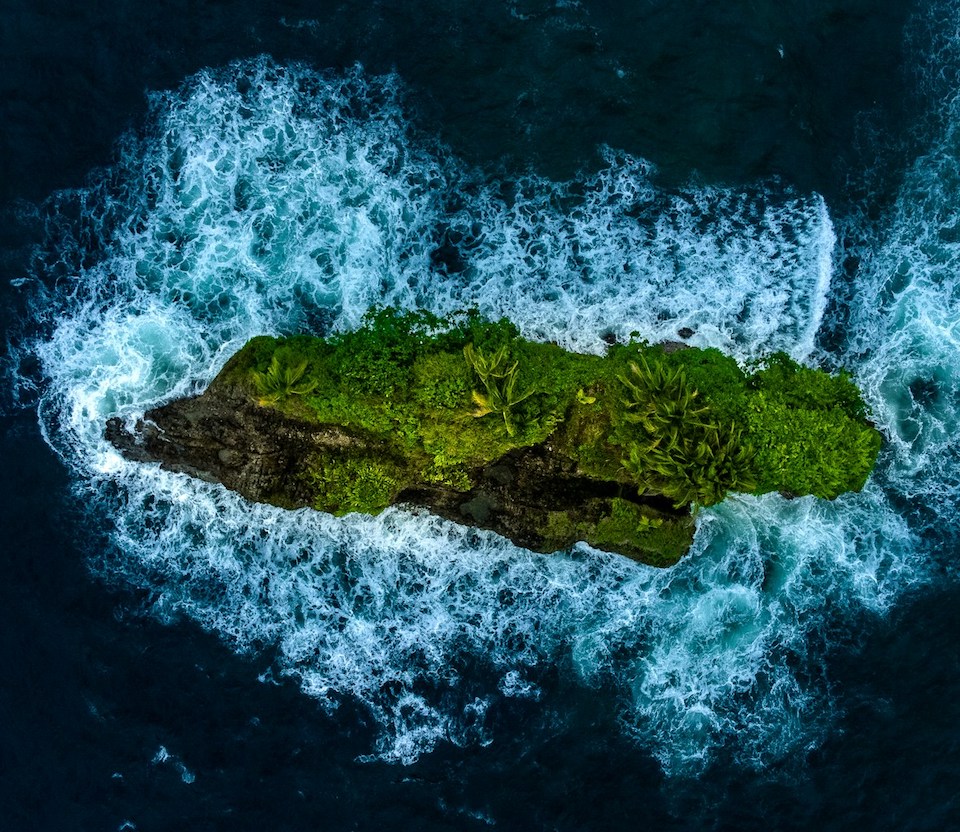 Aerial photograph of a lush, green island surrounded by dark blue sea, photo by Arne Tho