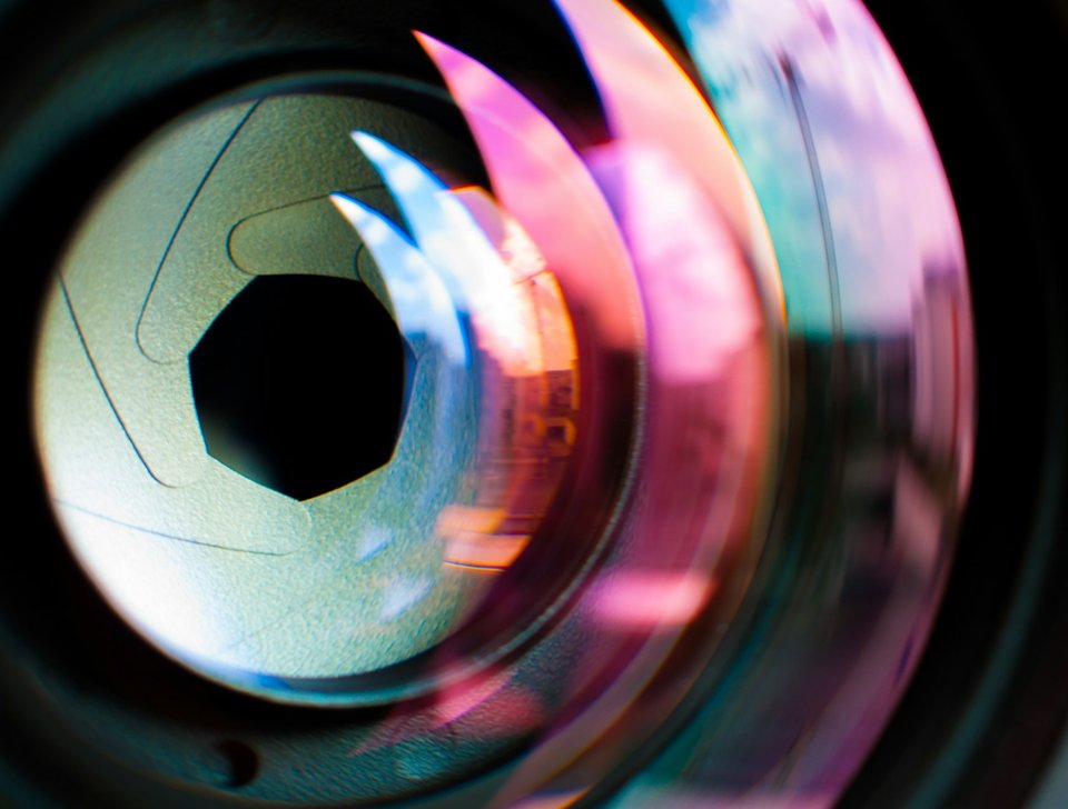 A close-up of a camera lens and diafragma with colourful reflections, photo by Agence Olloweb